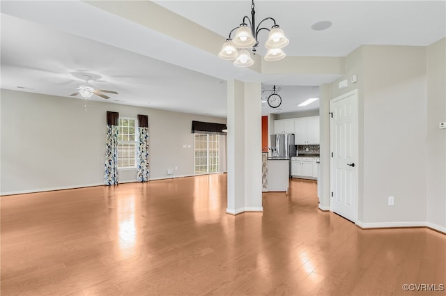 unfurnished living room with ceiling fan with notable chandelier and light hardwood / wood-style floors