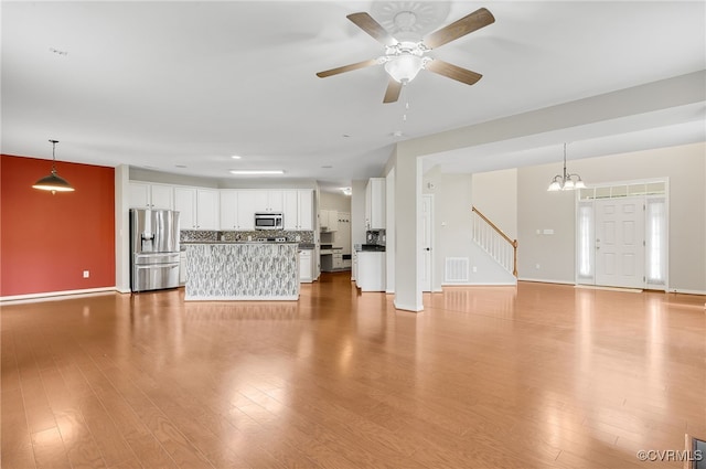 unfurnished living room with ceiling fan with notable chandelier and light hardwood / wood-style floors