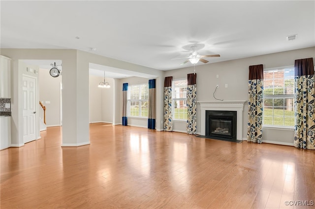 unfurnished living room featuring ceiling fan with notable chandelier and light wood-type flooring