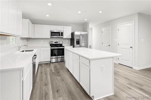 kitchen with a kitchen island, appliances with stainless steel finishes, white cabinetry, sink, and light hardwood / wood-style flooring