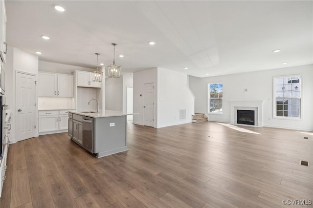 kitchen featuring decorative light fixtures, white cabinetry, sink, stainless steel dishwasher, and a center island with sink