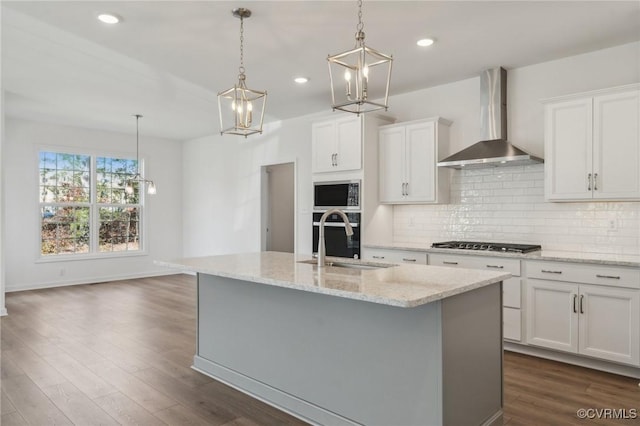 kitchen with wall chimney exhaust hood, decorative light fixtures, a center island with sink, and white cabinets