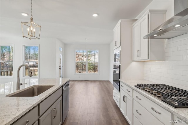 kitchen featuring white cabinetry, appliances with stainless steel finishes, light stone counters, and wall chimney range hood