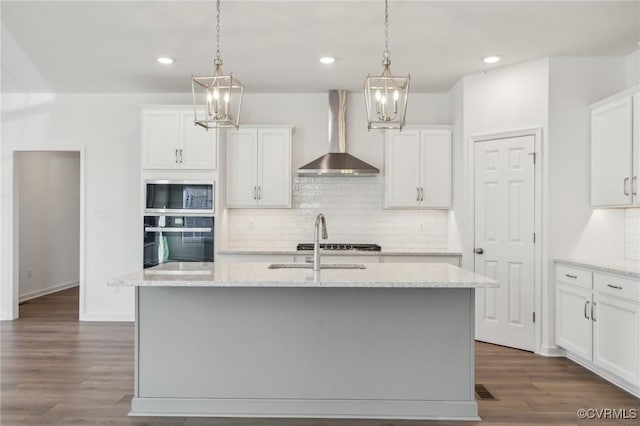 kitchen featuring white cabinets, a kitchen island with sink, and wall chimney range hood