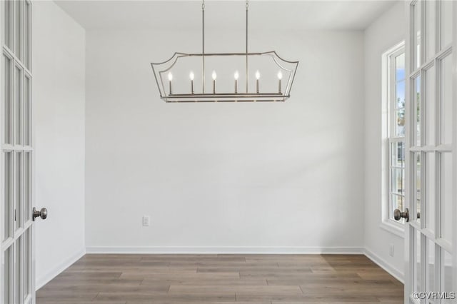 unfurnished dining area featuring french doors, a chandelier, and hardwood / wood-style flooring