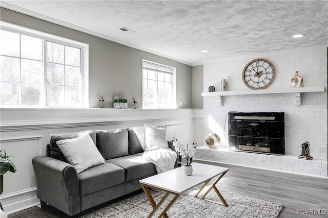 living room with a brick fireplace, hardwood / wood-style flooring, ornamental molding, and a textured ceiling