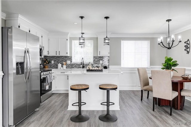 kitchen with appliances with stainless steel finishes, white cabinetry, hanging light fixtures, ornamental molding, and decorative backsplash