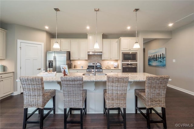 kitchen featuring stainless steel appliances, decorative light fixtures, sink, and a center island with sink