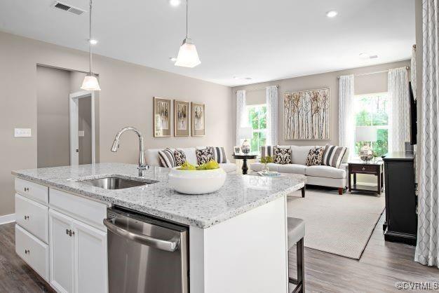 kitchen with pendant lighting, dishwasher, an island with sink, sink, and white cabinets