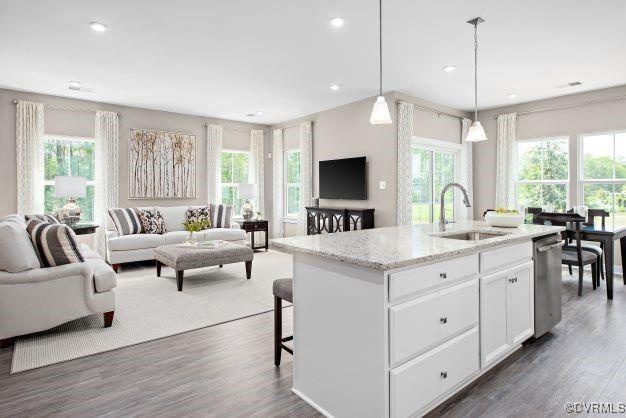 kitchen featuring white cabinetry, sink, hanging light fixtures, a kitchen island with sink, and light stone counters