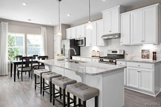 kitchen with stainless steel appliances, an island with sink, and white cabinets