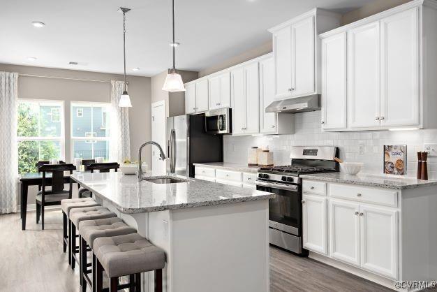 kitchen featuring decorative light fixtures, sink, white cabinets, stainless steel appliances, and a center island with sink