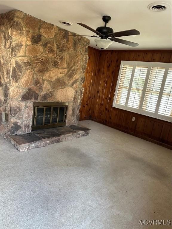 unfurnished living room with ceiling fan, carpet flooring, a stone fireplace, and wood walls