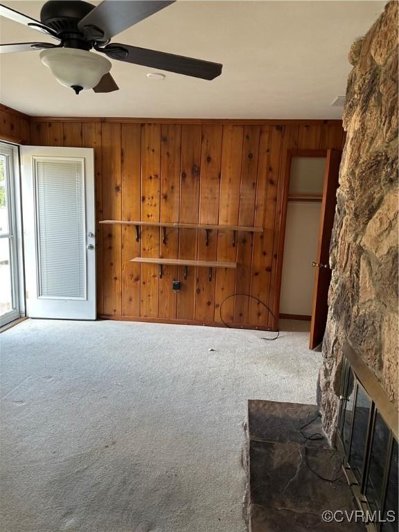 living room with a stone fireplace, wood walls, ceiling fan, and carpet flooring