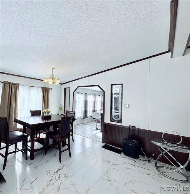 dining space with an inviting chandelier, wooden walls, crown molding, and a textured ceiling