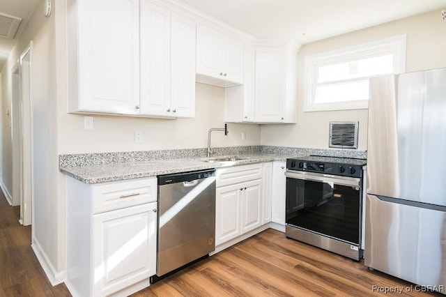 kitchen featuring appliances with stainless steel finishes, white cabinetry, sink, light hardwood / wood-style floors, and light stone countertops