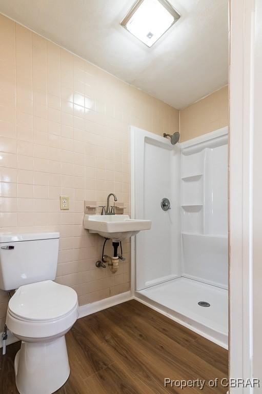 bathroom with wood-type flooring, a shower, sink, tile walls, and toilet