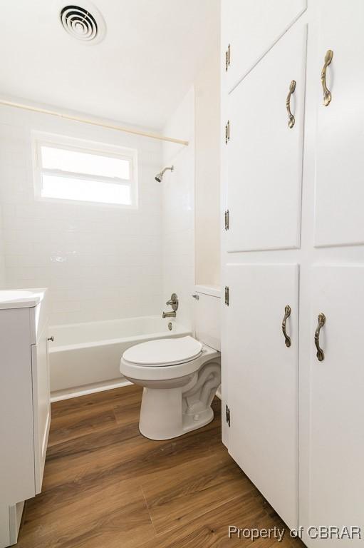 full bathroom featuring vanity, hardwood / wood-style flooring, tiled shower / bath combo, and toilet