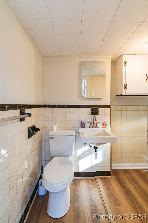 bathroom featuring wood-type flooring, toilet, sink, and tile walls