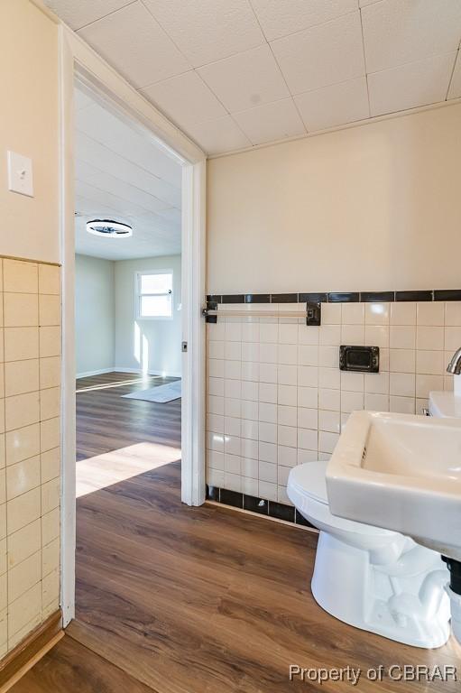 bathroom featuring hardwood / wood-style flooring, toilet, and tile walls