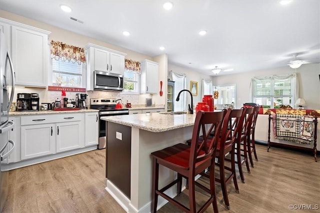 kitchen featuring sink, appliances with stainless steel finishes, light stone countertops, white cabinets, and a center island with sink