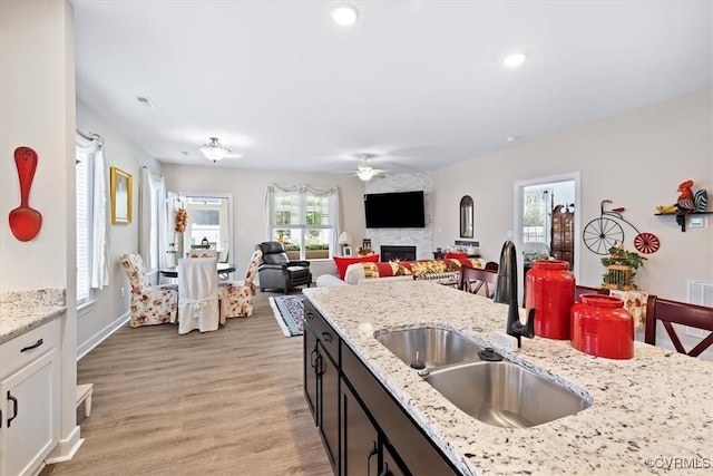 kitchen featuring sink, white cabinetry, light hardwood / wood-style flooring, a large fireplace, and light stone countertops