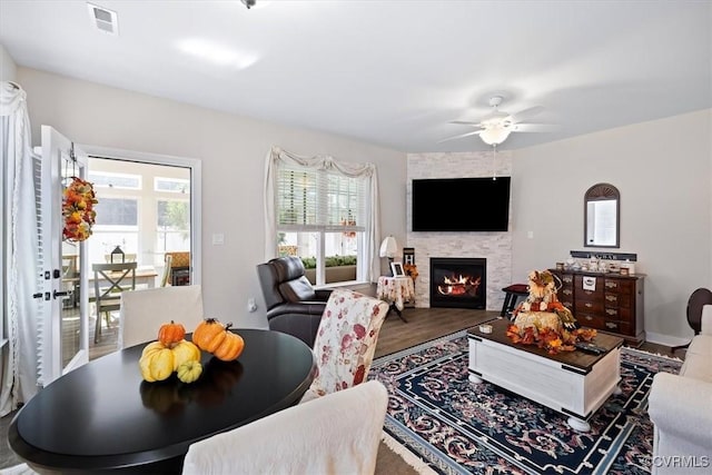 living room with wood-type flooring, a stone fireplace, and ceiling fan