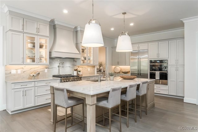 kitchen with stainless steel built in refrigerator, sink, custom exhaust hood, an island with sink, and black double oven