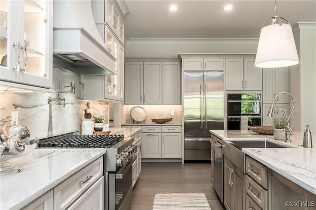 kitchen featuring premium range hood, sink, tasteful backsplash, premium appliances, and pendant lighting