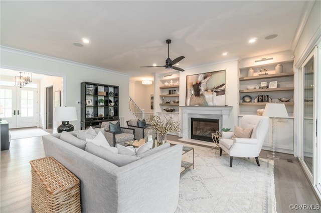 living room featuring crown molding, light hardwood / wood-style flooring, ceiling fan, built in shelves, and french doors