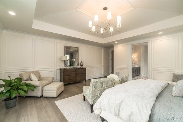 bedroom featuring wood-type flooring, a tray ceiling, ensuite bathroom, and a notable chandelier