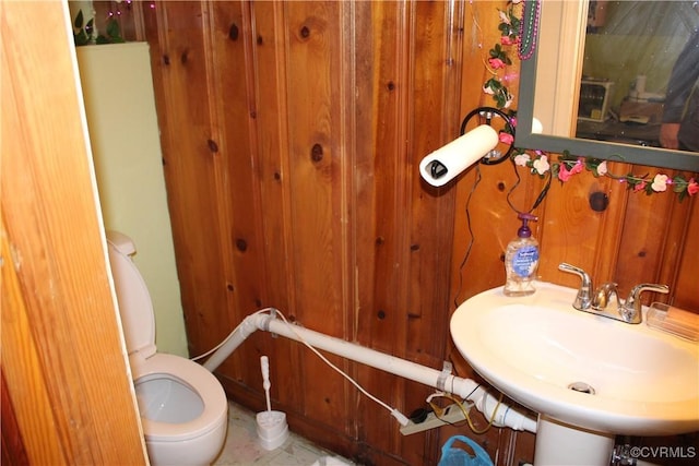 bathroom featuring sink, wooden walls, and toilet