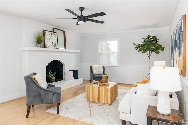 living room with crown molding, ceiling fan, wood-type flooring, and a fireplace