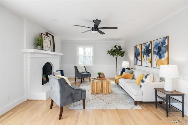 living room with hardwood / wood-style flooring, ceiling fan, crown molding, and a brick fireplace