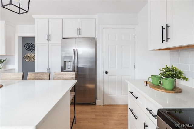 kitchen with stainless steel fridge, a breakfast bar, white cabinetry, hanging light fixtures, and light wood-type flooring