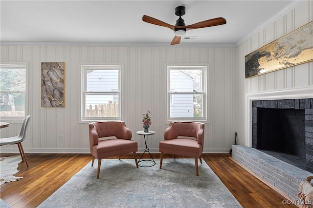 living area with ornamental molding, a brick fireplace, dark hardwood / wood-style floors, and ceiling fan