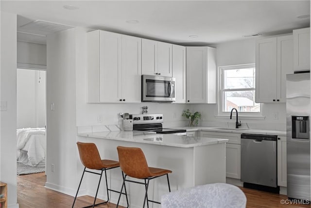 kitchen featuring appliances with stainless steel finishes, sink, white cabinets, dark hardwood / wood-style flooring, and kitchen peninsula