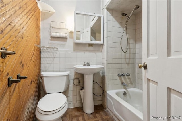 full bathroom with toilet, sink, tiled shower / bath, tile walls, and parquet floors