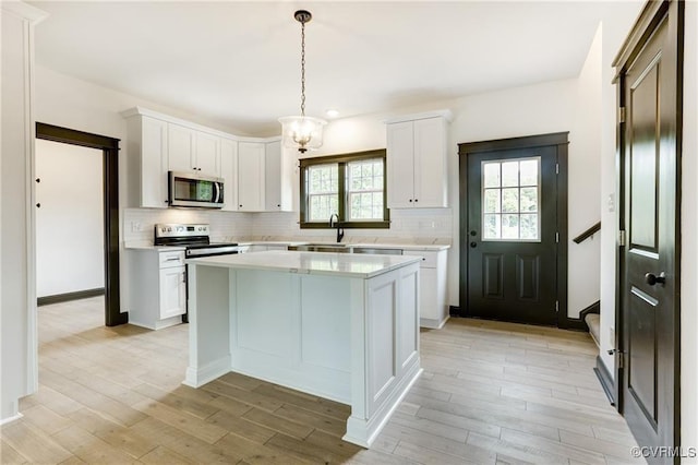 kitchen with tasteful backsplash, a center island, appliances with stainless steel finishes, pendant lighting, and white cabinets