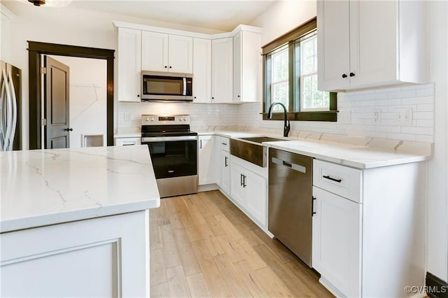 kitchen with sink, light stone counters, stainless steel appliances, light hardwood / wood-style floors, and white cabinets