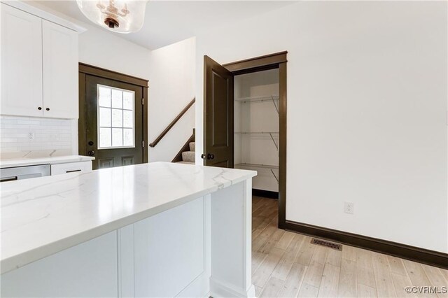 kitchen featuring tasteful backsplash, light stone countertops, light hardwood / wood-style floors, and white cabinets