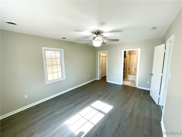 unfurnished bedroom featuring ensuite bath, dark wood-type flooring, ceiling fan, a spacious closet, and a closet