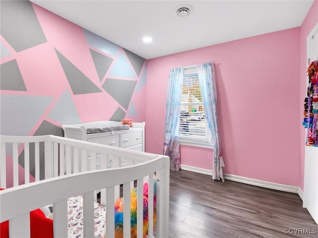 bedroom with a nursery area and dark hardwood / wood-style floors