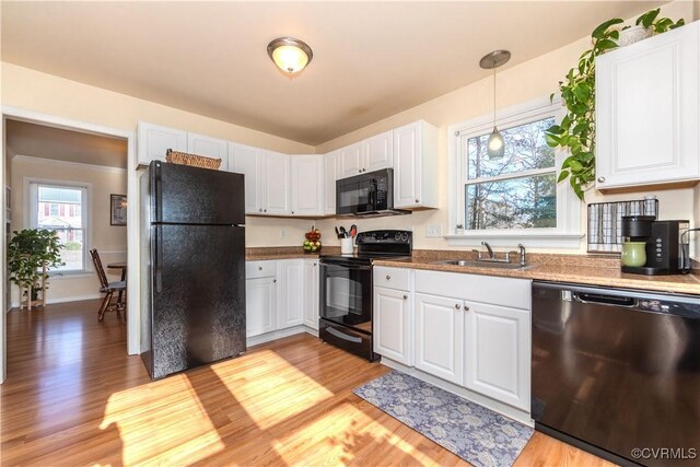 kitchen featuring pendant lighting, sink, white cabinetry, black appliances, and light wood-type flooring