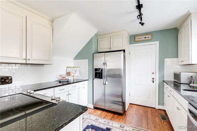 kitchen with backsplash, appliances with stainless steel finishes, light hardwood / wood-style floors, and dark stone counters