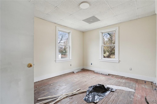 empty room featuring wood-type flooring, plenty of natural light, and a drop ceiling