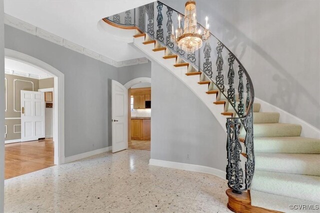 stairway with arched walkways, an inviting chandelier, baseboards, and tile patterned floors