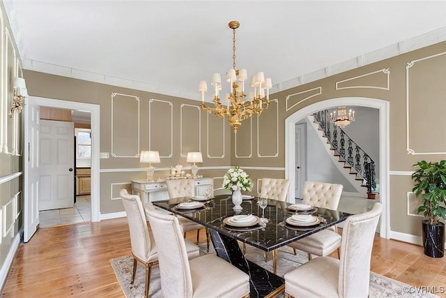 dining area featuring light wood-style floors, stairs, a chandelier, and arched walkways