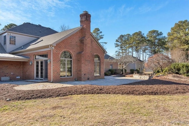 rear view of house featuring a yard, brick siding, a patio, and a chimney