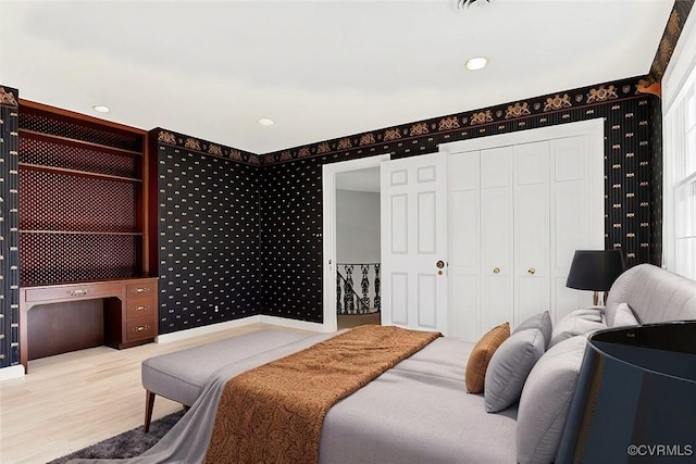 bedroom with a closet, wood finished floors, baseboards, and wallpapered walls